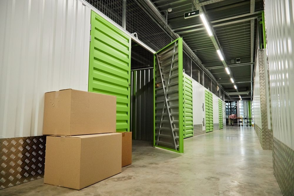 Storage units in a hallway with boxes. Green doors and white walls with gray concrete floor. — Gympie Southside Mini Storage in Southside, QLD