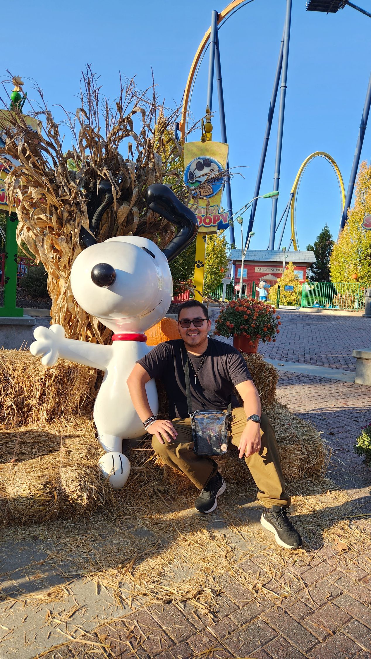 A man is sitting on a bale of hay next to a statue of snoopy.