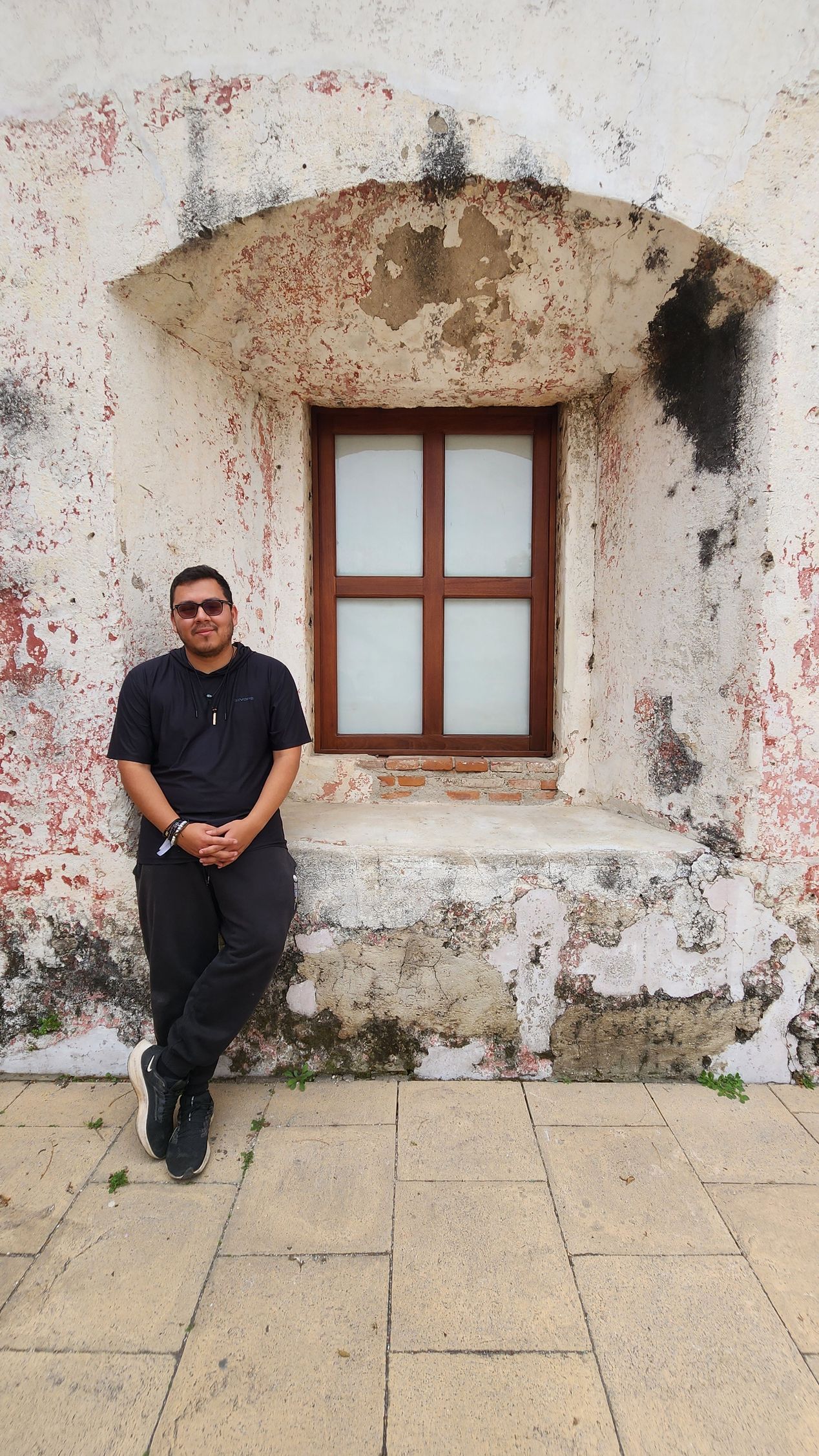 A man is leaning against a wall next to a window.