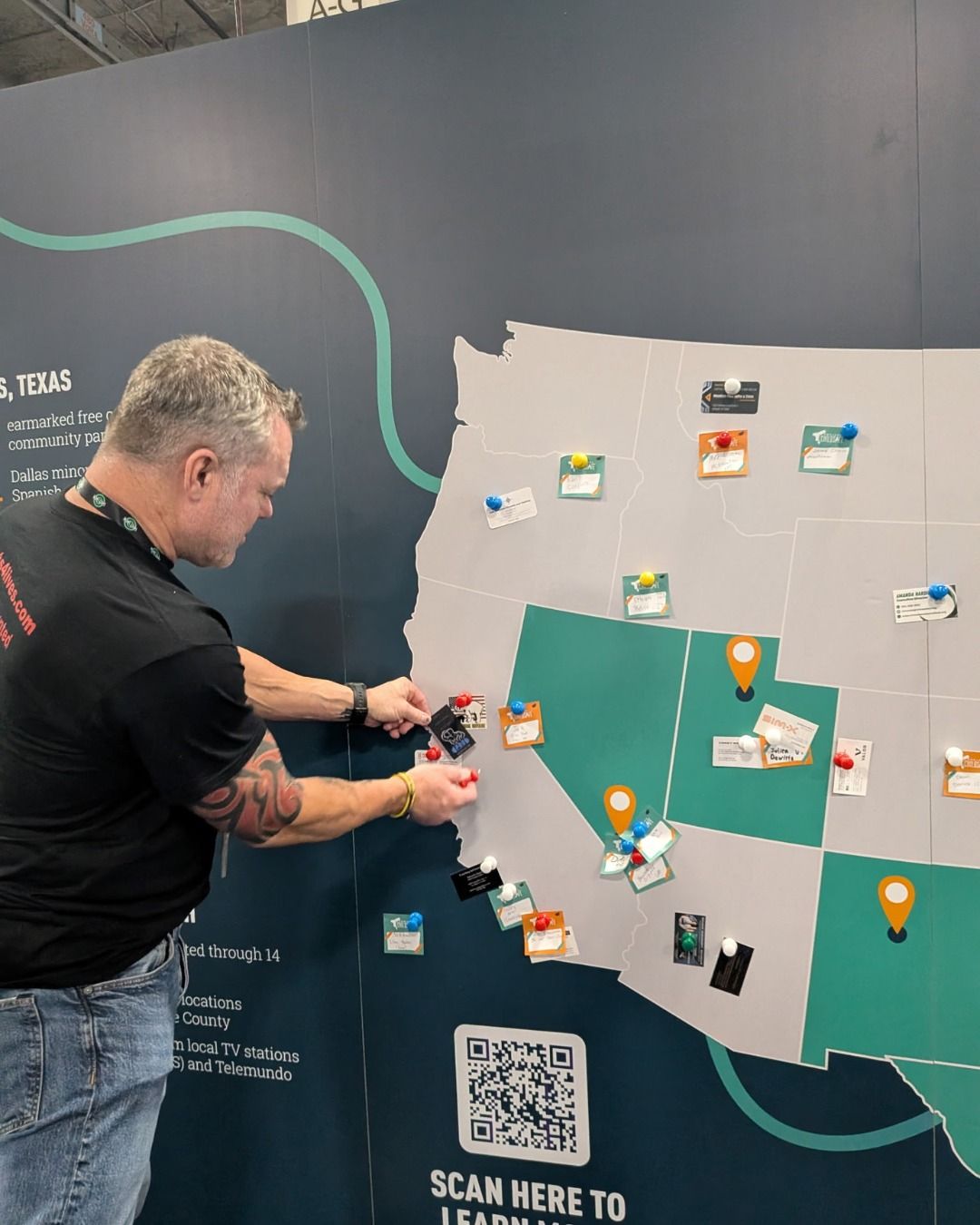 A person pins a small card to a large wall map of the western United States at a trade show exhibit.