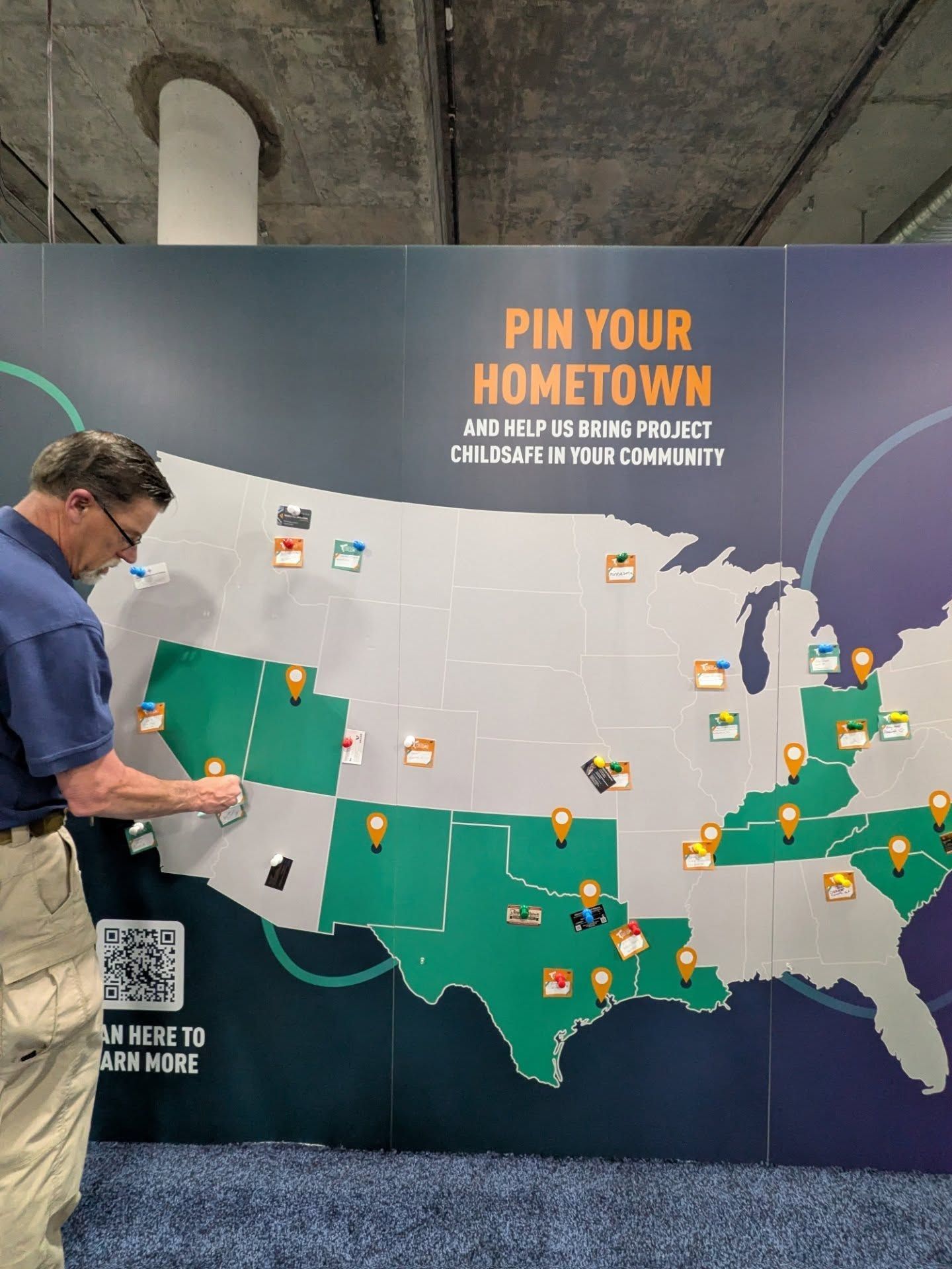 A man places a pin on a map of the United States on a wall display titled