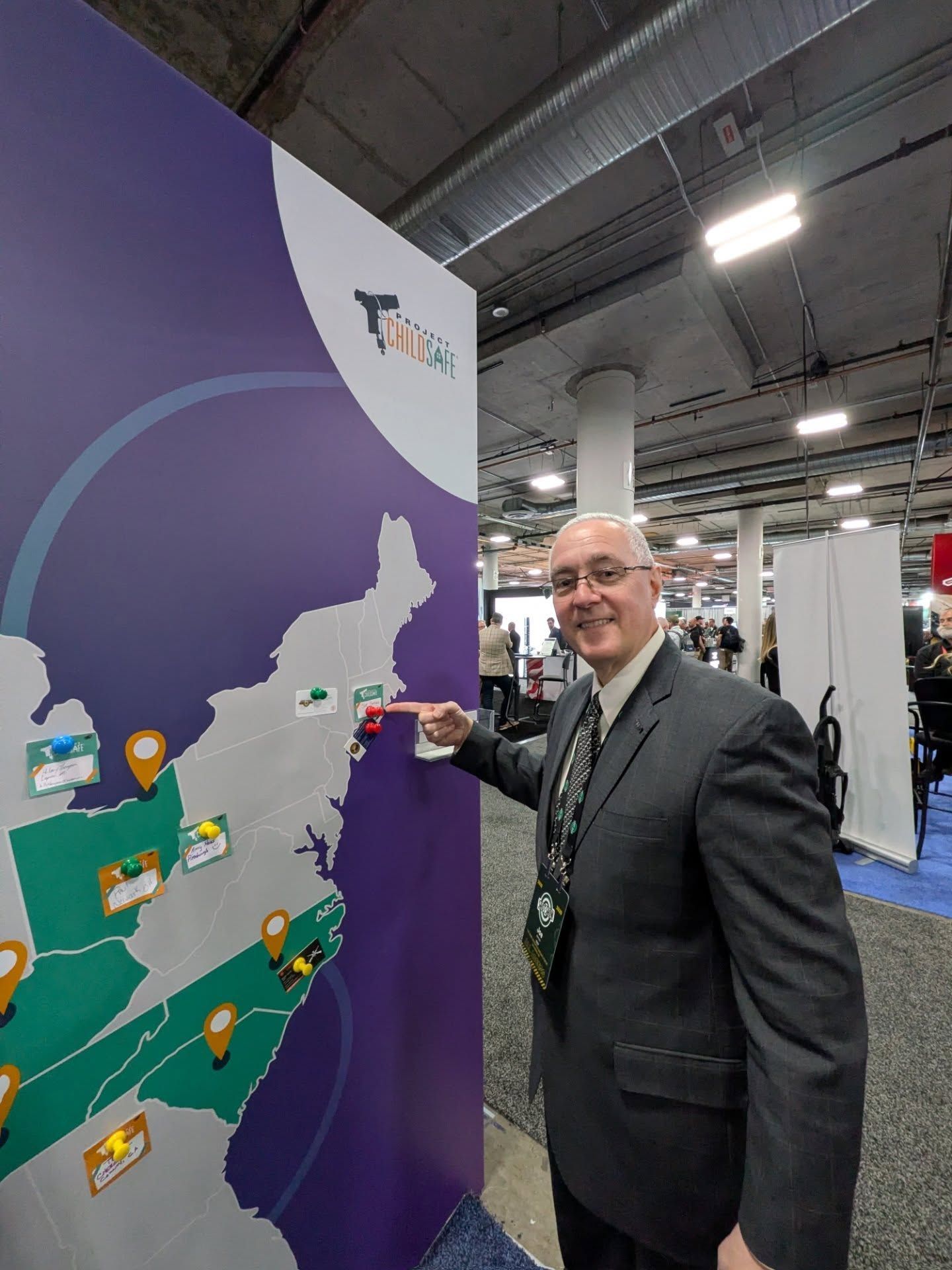 A smiling person in a suit pointing to a map of the eastern United States on a large display at a conference.