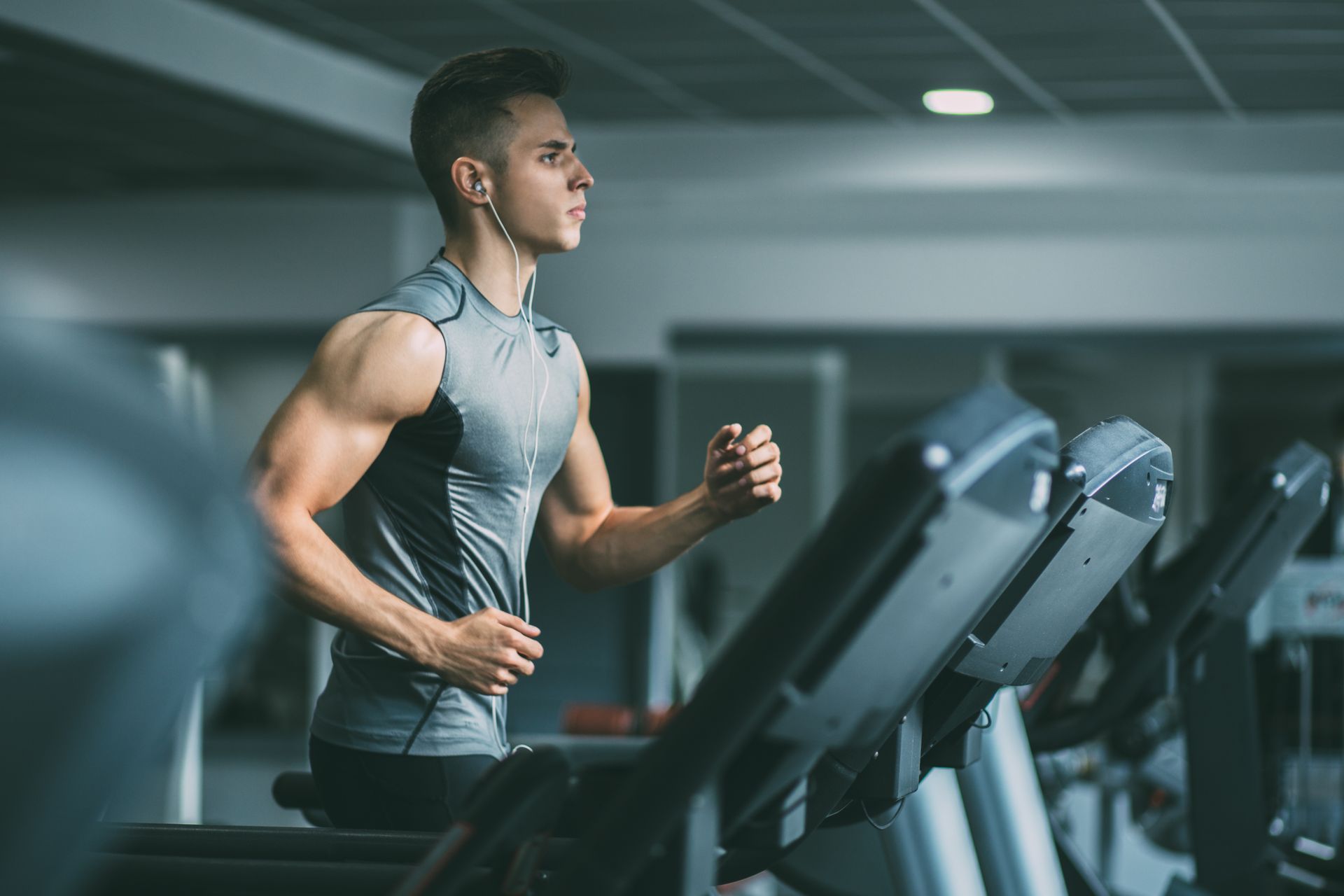 Man running on a treadmill at a gym, wearing a gray workout shirt.
