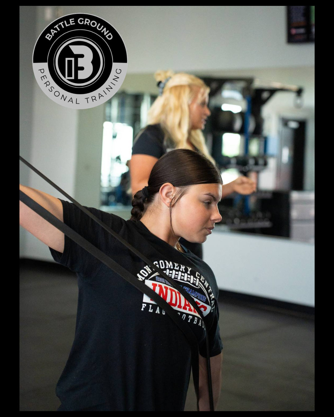 Woman using resistance band for exercise; instructor watches in gym setting.