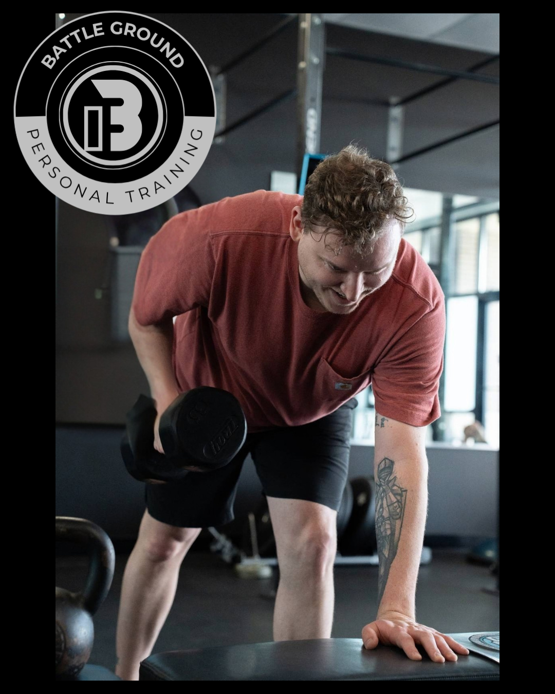 Man lifting dumbbell in a gym. Red shirt, black shorts. Holding weight, focused expression. Battle Ground logo.