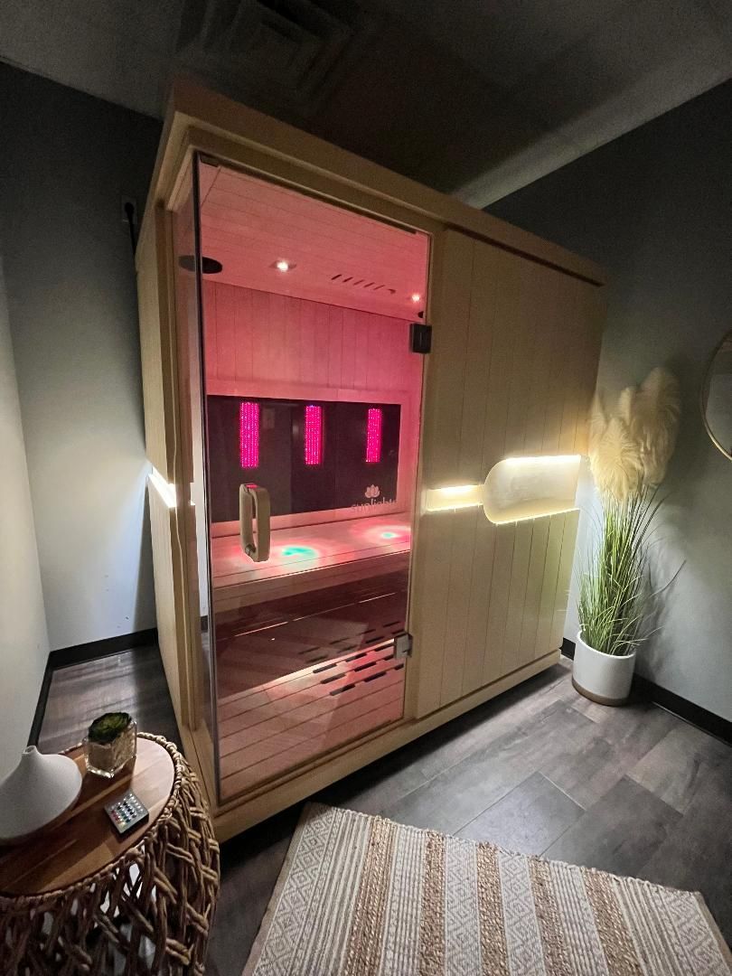 A modern wooden home sauna with a glass front, glowing pink interior lighting, and ambient LED wall accents in a room.