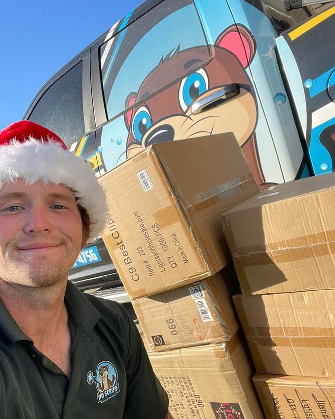 A man wearing a santa hat is standing next to a pile of cardboard boxes.