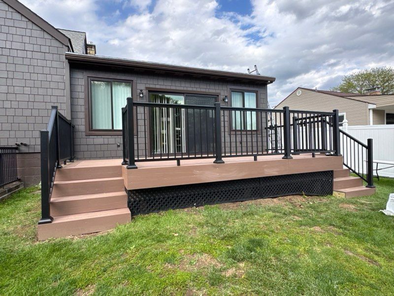 Backyard deck with black railing, tan steps, and sliding glass doors on a gray house