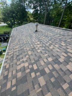 Asphalt shingle roof with a mottled brown and gray pattern; vent pipe in the center.