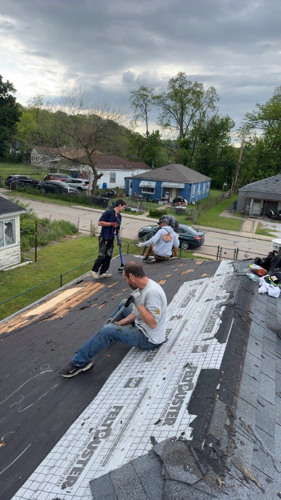 Workers repairing a shingled roof with houses and trees in the background