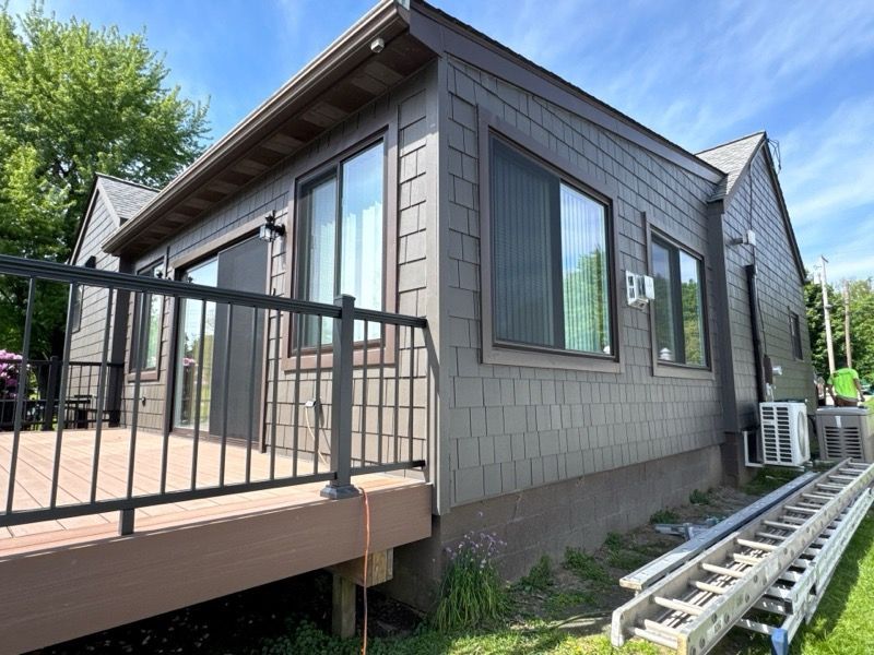 Small house exterior with a deck, black railing, gray siding, and a ladder along the side yard