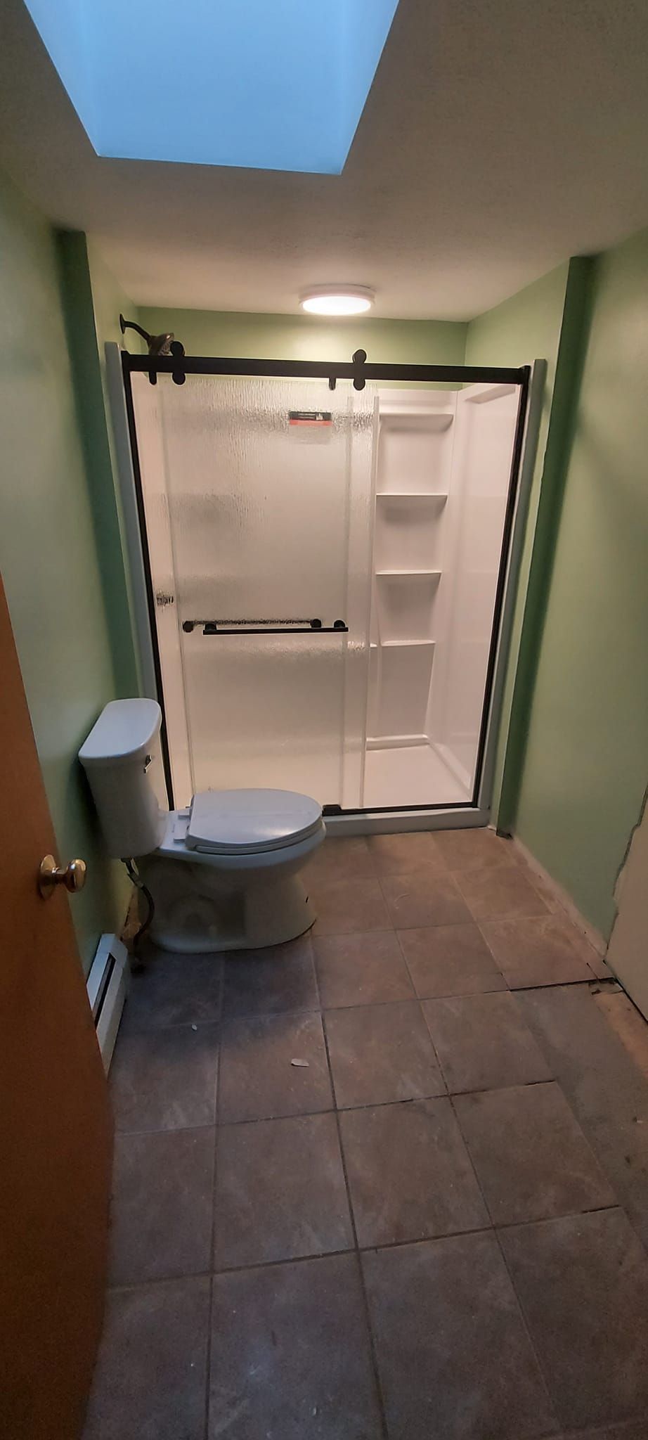 A bathroom with a toilet , shower and skylight.