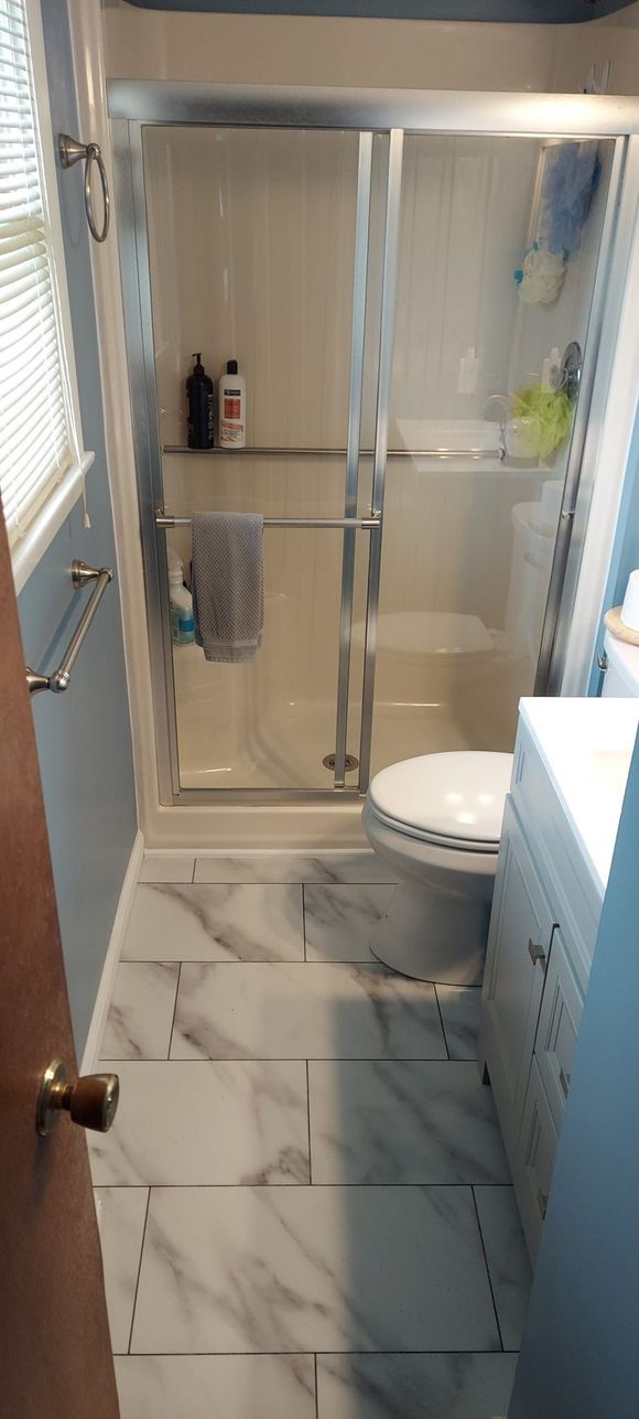 A bathroom with a toilet , shower , sink and window.