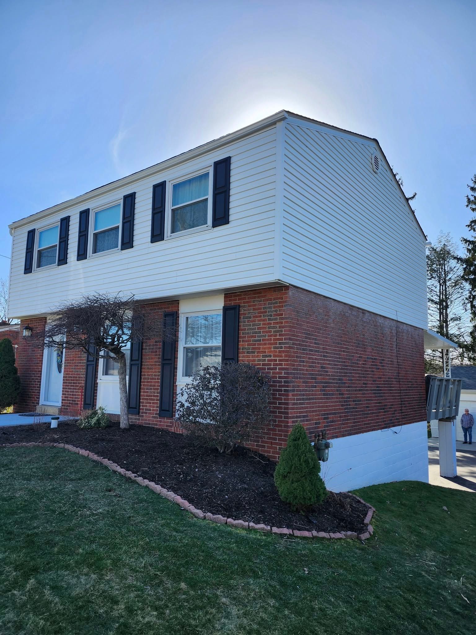 A brick house with a white siding and black shutters on a sunny day.