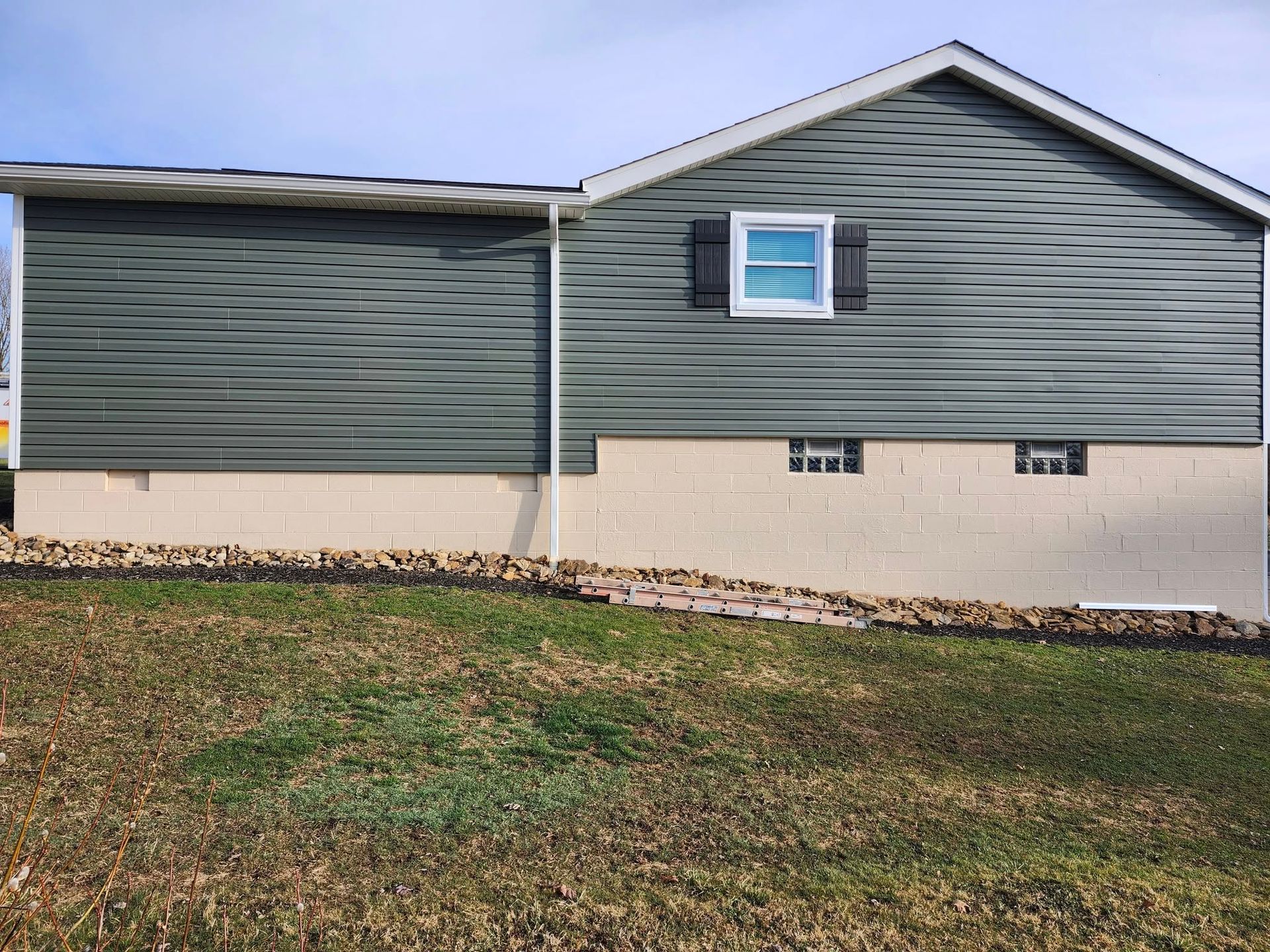 A house with a green siding and a white roof is sitting on top of a grassy hill.
