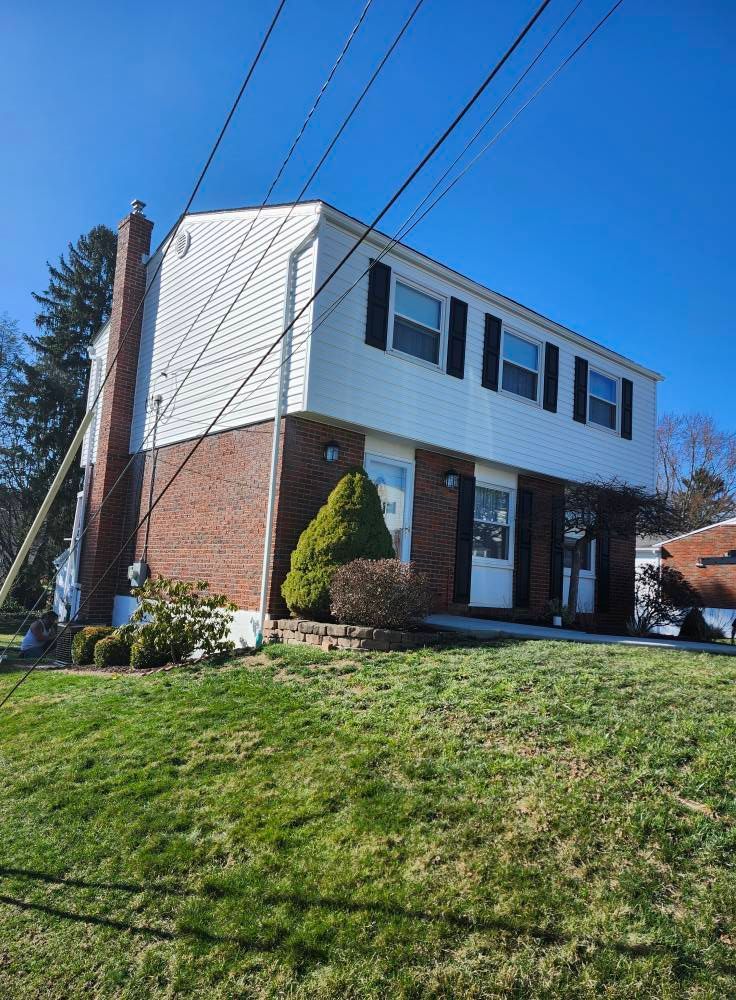A brick house with a white siding and black shutters on a sunny day.