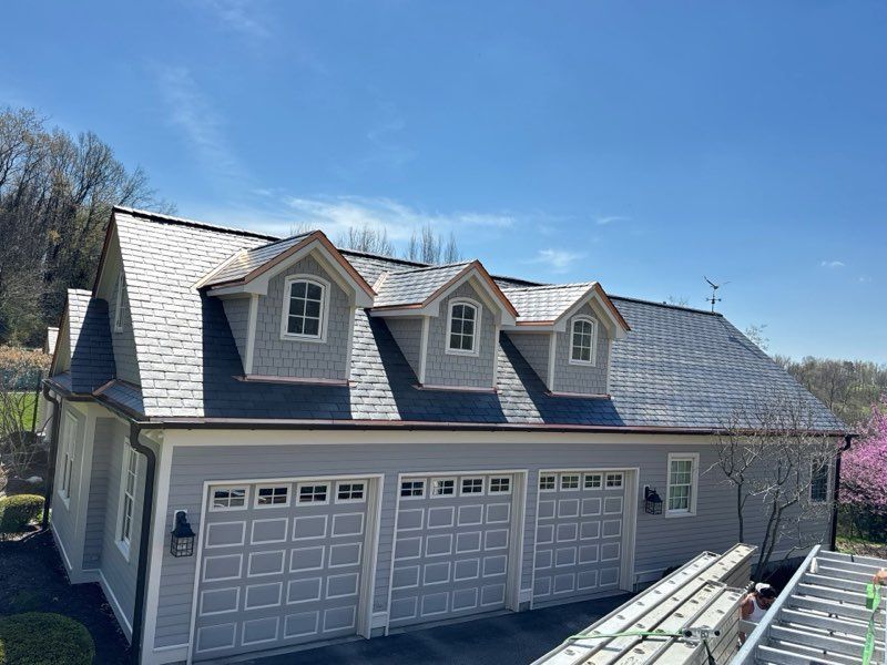 Three-car garage with gray siding and dormer windows under a blue sky