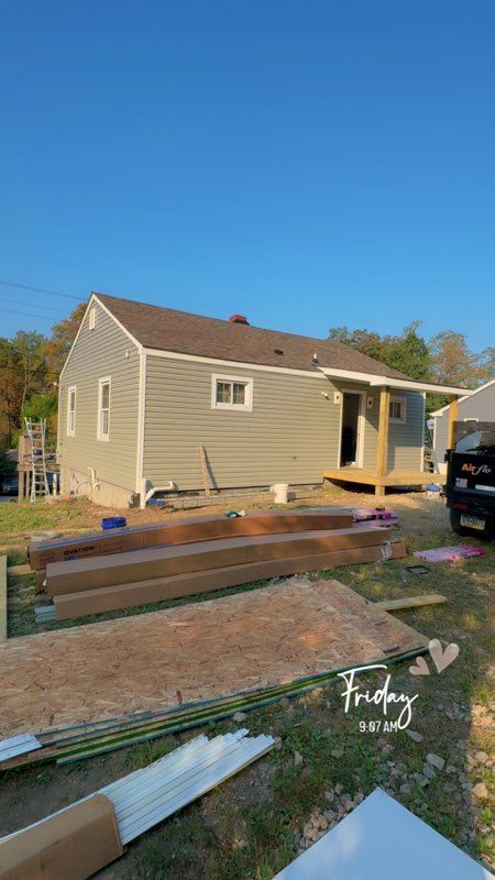 Construction site with a house, building materials, and a small deck under construction, with a clear sky.