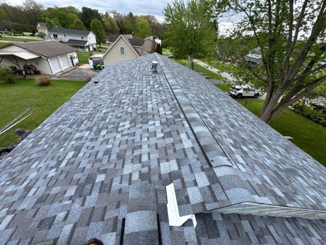Roof with gray shingles and a loose vent pipe in a suburban neighborhood