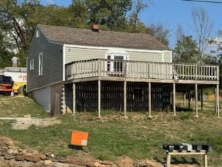 Gray house with a raised wooden deck on a grassy hill; a work truck is visible in the background.