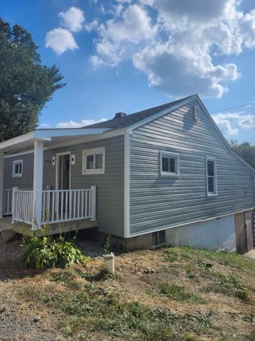Gray-sided house with white trim, porch, and windows; set against a blue sky with clouds.