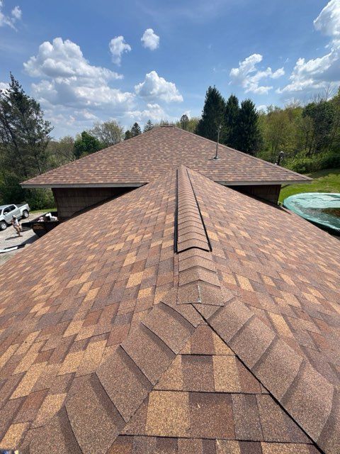 Close-up of a brown shingle roof ridge under a blue sky with clouds