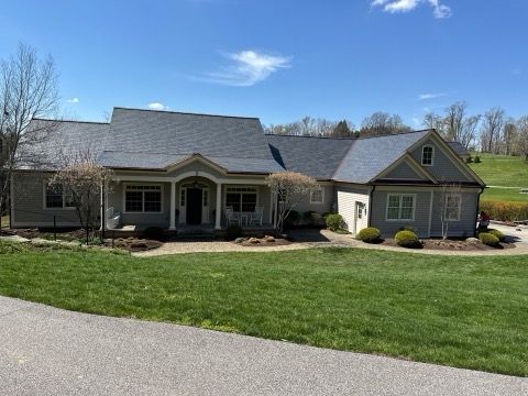 Single-story suburban house with gray roof, front porch, green lawn, and blue sky