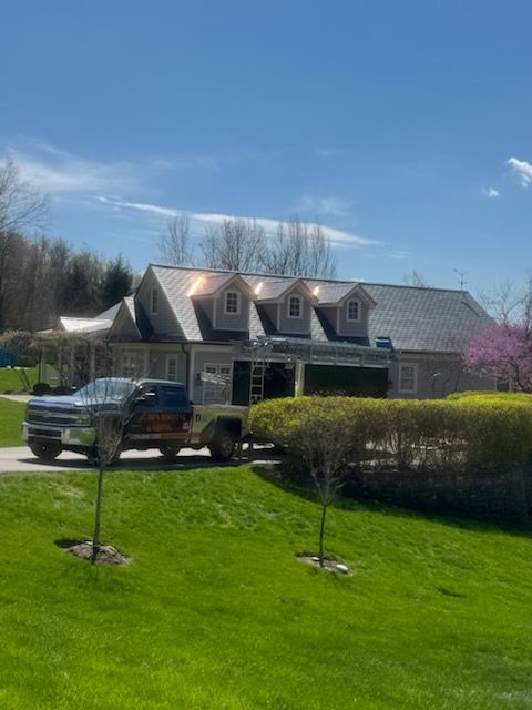 Suburban house with gray roof, black pickup truck in driveway, and bright green lawn under a blue sky