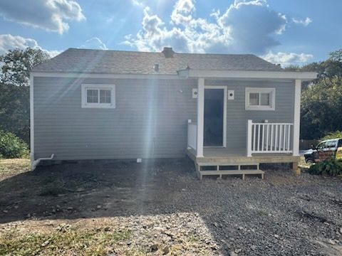 Gray-sided small house with a porch and steps, windows, and a dark front door, under a sunny sky.