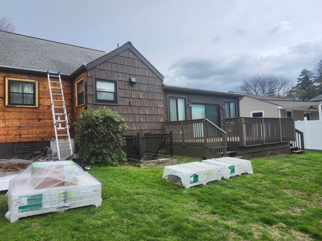 Backyard with a wooden house, deck, and two wrapped pallets on the grass under a cloudy sky