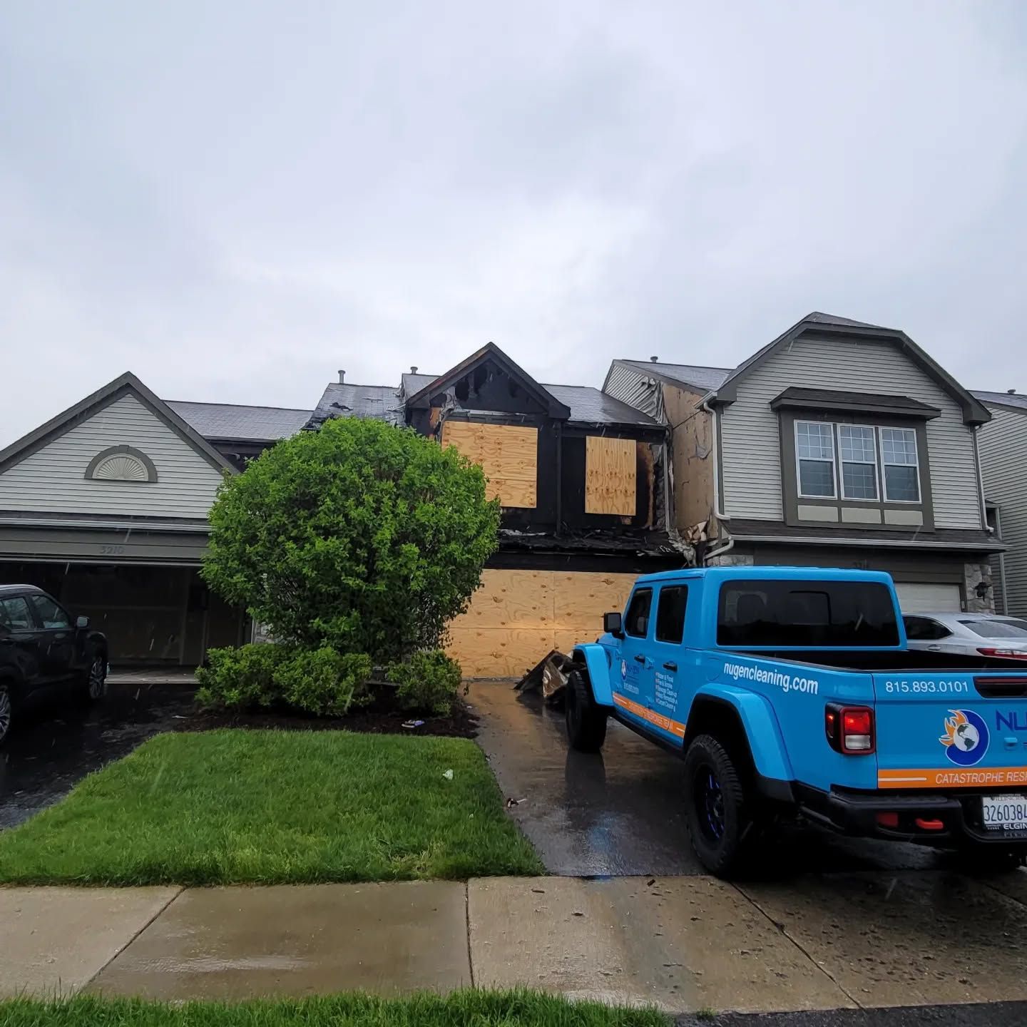 A blue truck is parked in front of a house that has been damaged by a fire.