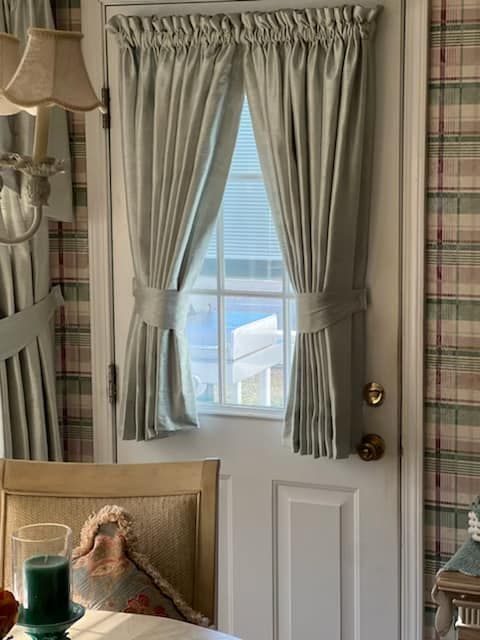 Curtains on a door with plaid wallpaper.