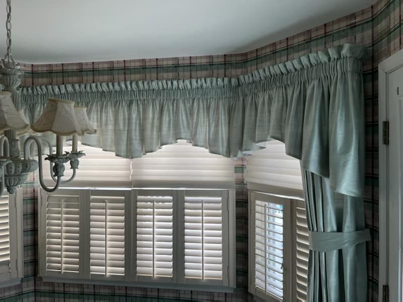 A valance, shades, and shutters on a bay window.