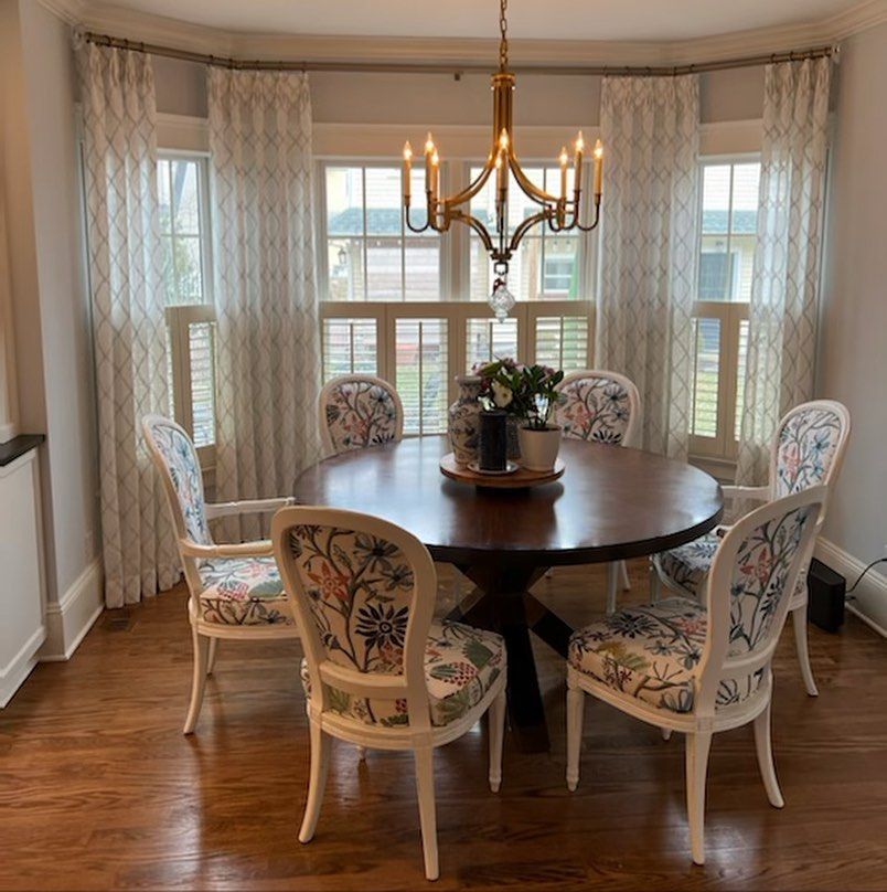 A dining room table and chairs in front of a bay window with drapery