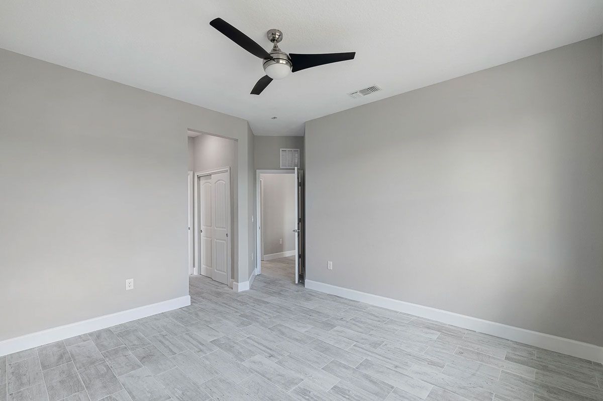 An empty bedroom with a ceiling fan in the corner.