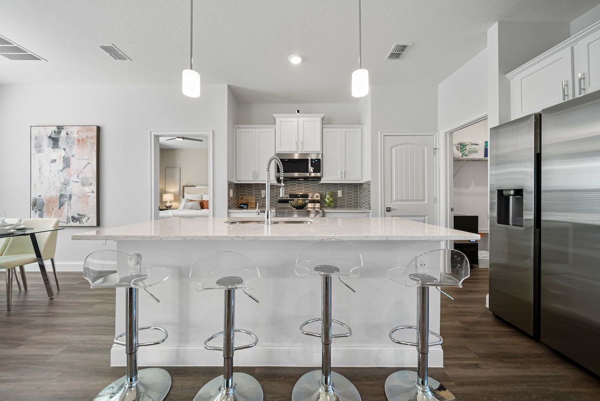 A kitchen with white cabinets , stainless steel appliances , a large island and stools.