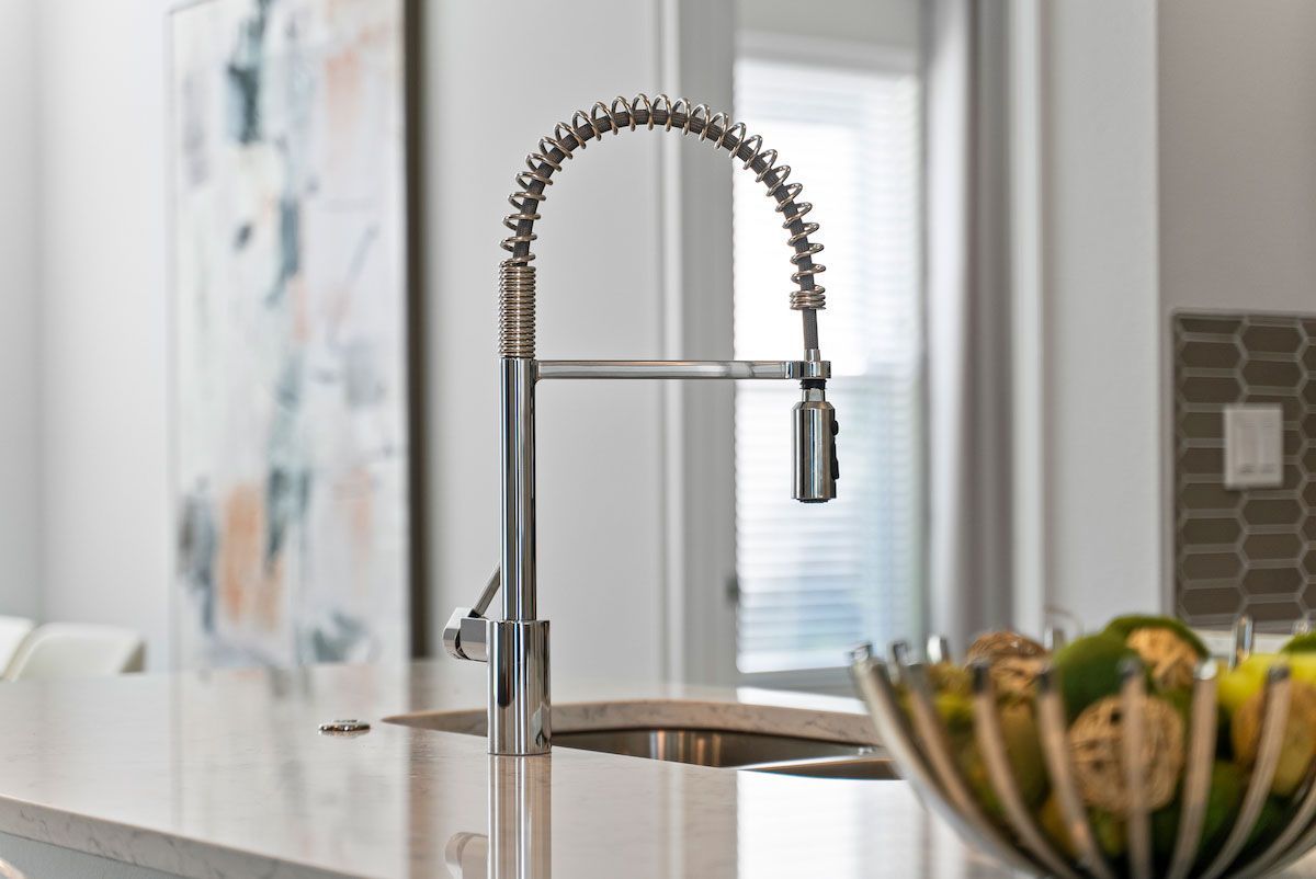 A kitchen sink with a faucet and a bowl of fruit on the counter.