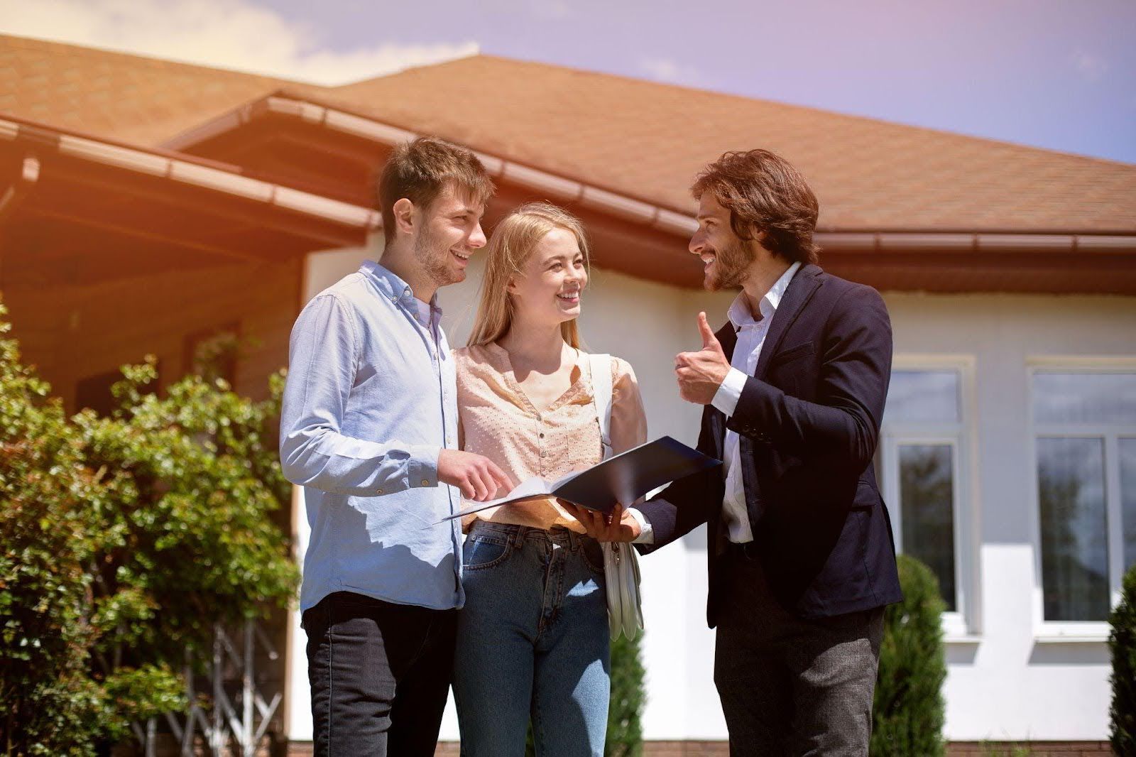 A young couple talks with a real estate agent in front of a new home in Palm Coast, smiling and hold