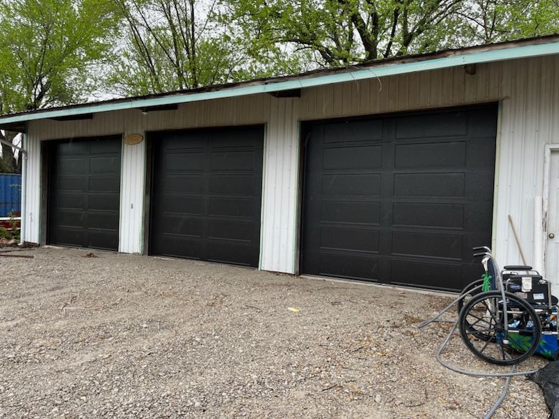 A garage with three new black garage doors and a wheelchair in front of it.
