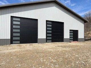 A white building with black garage doors is sitting on top of a dirt field.
