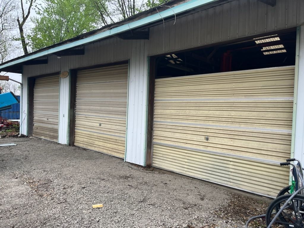 A row of garage doors with a bicycle parked in front of them. The garage doors are yellow and dirty, and one has a gap.
