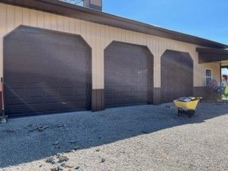 A house with three garage doors and a yellow wheelbarrow in front of it.