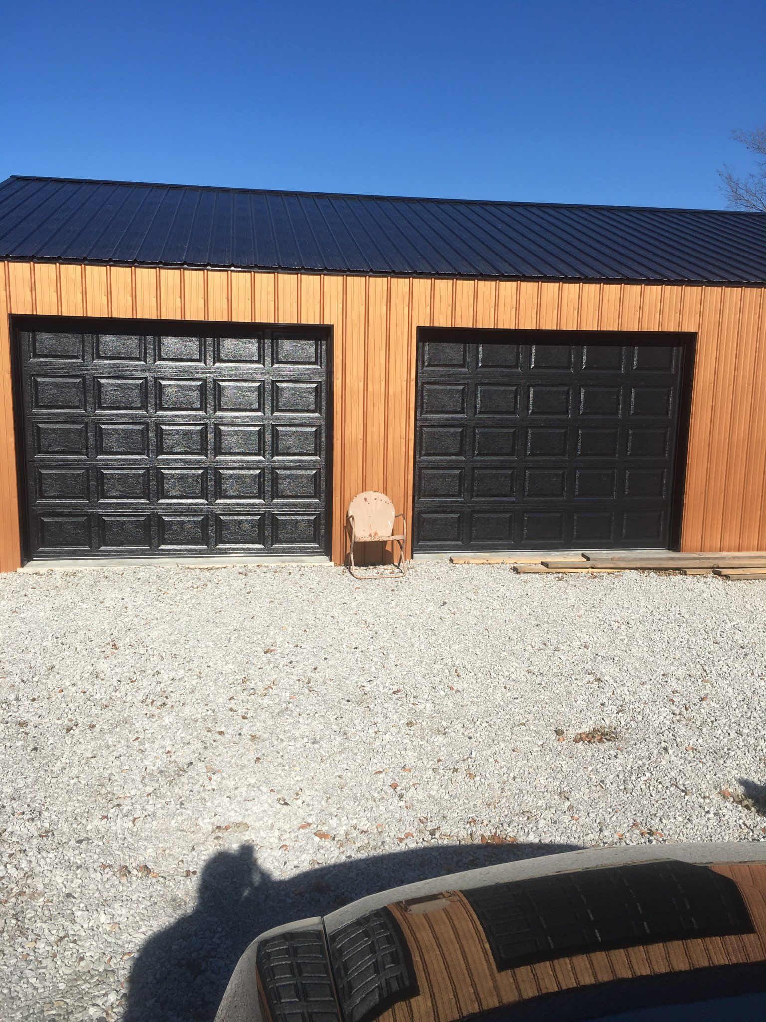 A car is parked in front of a garage with two black garage doors.
