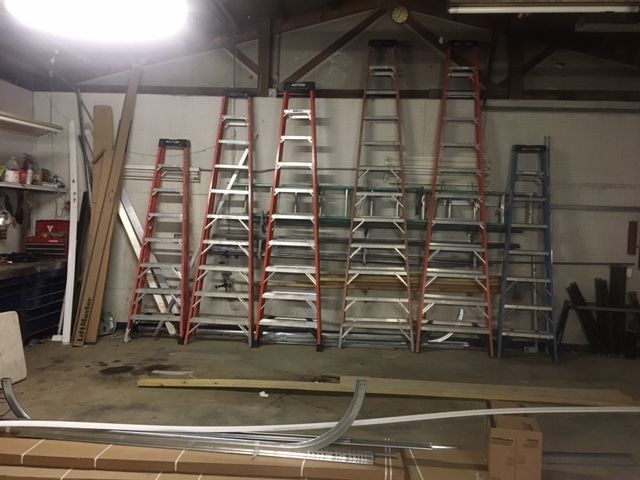 A bunch of ladders are lined up in a garage