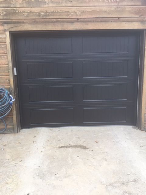 A black garage door is sitting in front of a wooden building.