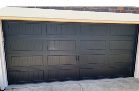 A black garage door is sitting in front of a brick building.
