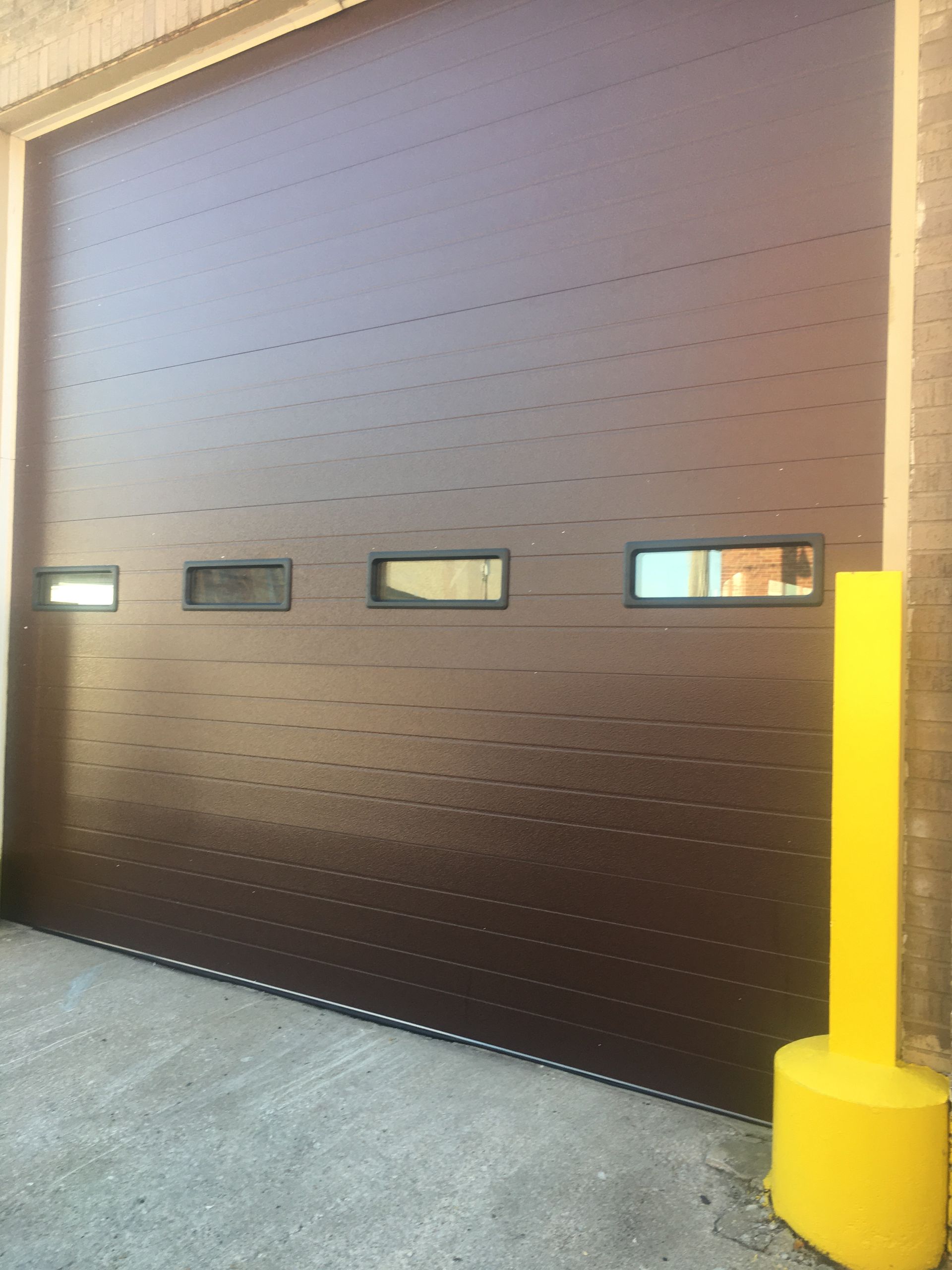 A brown garage door with a yellow pole in front of it.