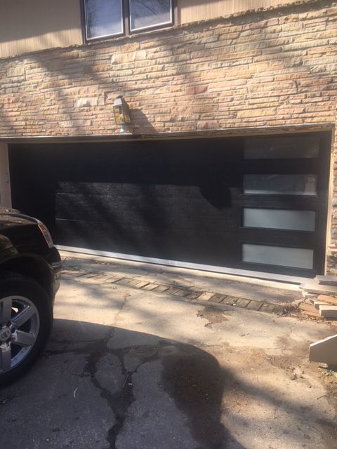 A black car is parked in front of a brick garage door.