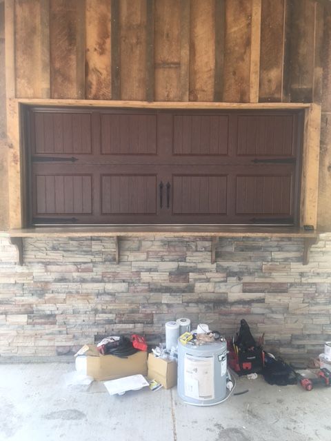 A brown garage door is sitting in front of a brick wall.