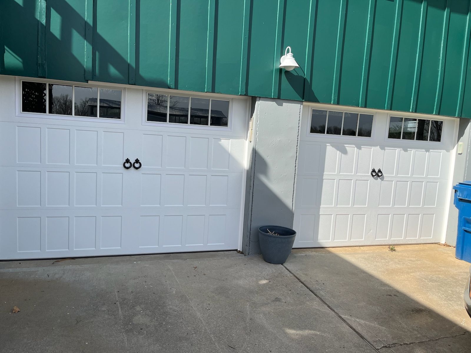 Two white garage doors are sitting next to each other in front of a green building.